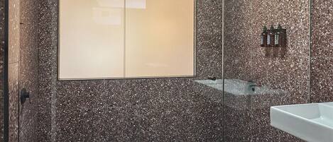 A modern shower area with a glass enclosure, a large mirror, and a tiled floor.