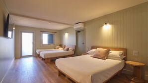 A hotel room with two single beds, a large bed, wooden flooring, a window, and an air conditioning unit. - Alpine Inn (Khancoban)