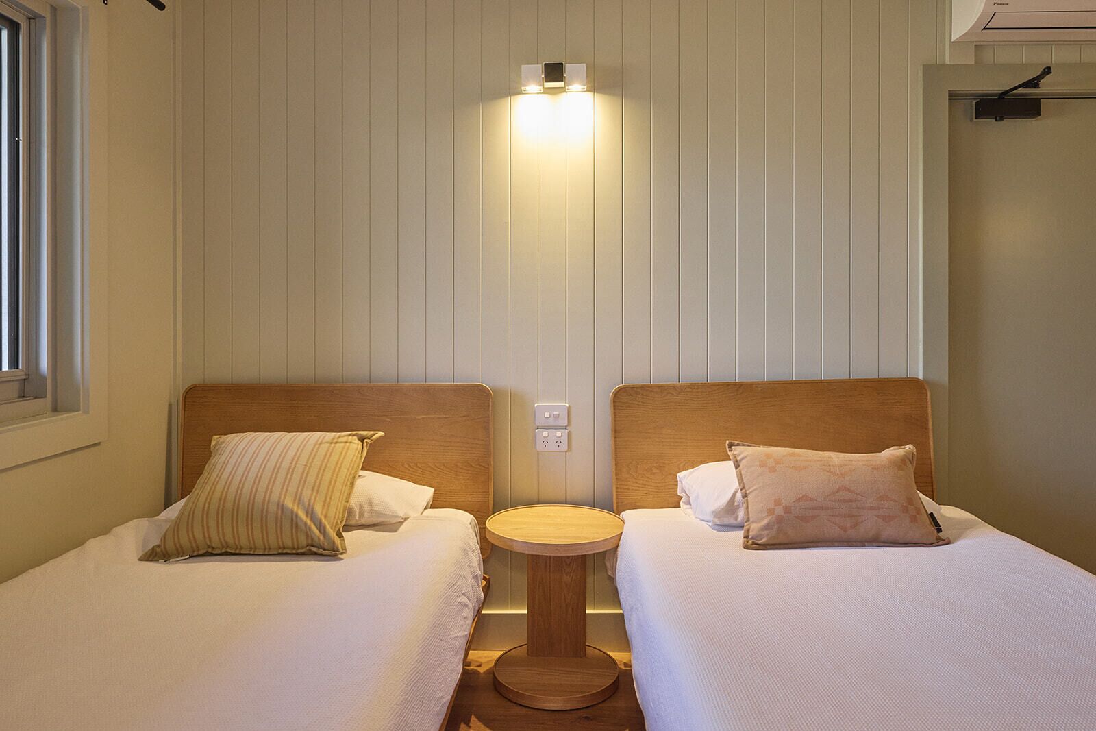 A twin room with two beds, a small round table, and a wall-mounted light fixture.