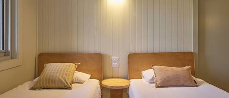 A twin room with two beds, a small round table, and a wall-mounted light fixture.