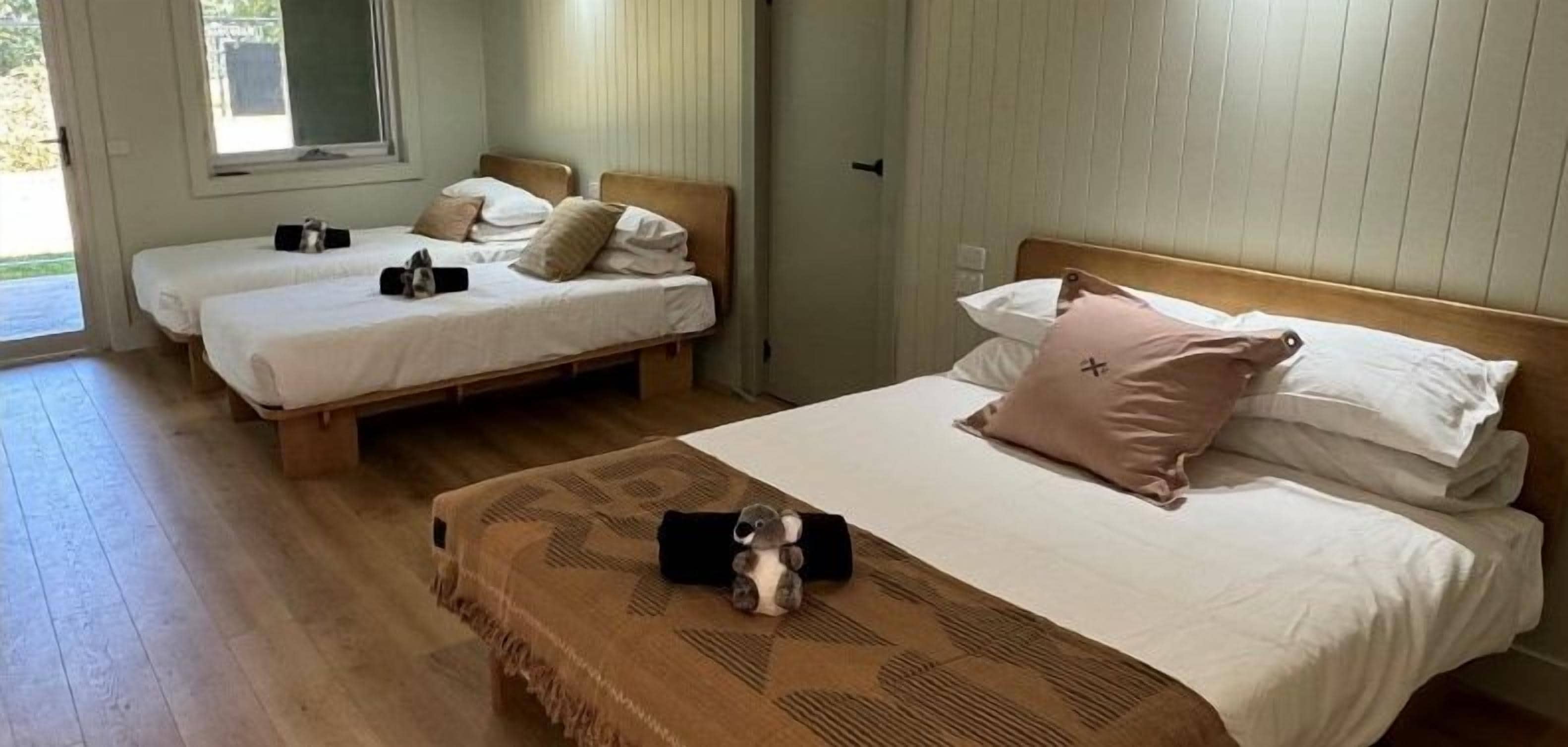 Habitación de hotel con dos camas individuales y una cama grande, con piso de madera.