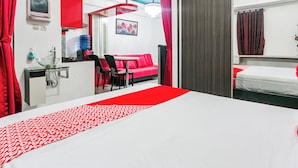 A hotel room with a bed, a sofa, a desk with a chair, a water dispenser, and a red curtain. - Hotel O Mp Room (Depok)