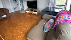 Ett vardagsrum med en brun lädersoffa, en platt-TV på ett träställ och ett stort fönster med gardiner.