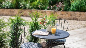 Une table ronde sur laquelle se trouvent un livre, une paire de lunettes, un vase avec une fleur et un verre de jus d’orange.