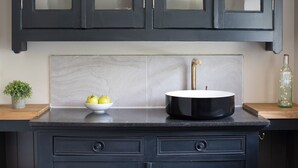 Une cuisine avec un plan de travail noir, un saladier blanc rempli de pommes, un évier noir et une bouteille verte.