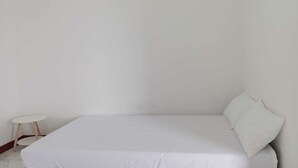Una habitación sencilla y sin adornos, con una cama, una mesita redonda y una pared lisa.