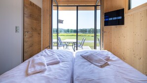 Una camera da letto con due letti, una TV a parete e una porta vetrata scorrevole che dà su un’area salotto all’aperto.
