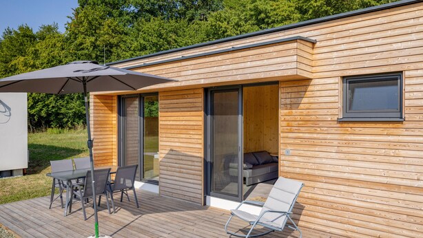 Un'accogliente baita in legno dalle linee moderne con terrazza, tavolo e sedie, e una poltrona relax.