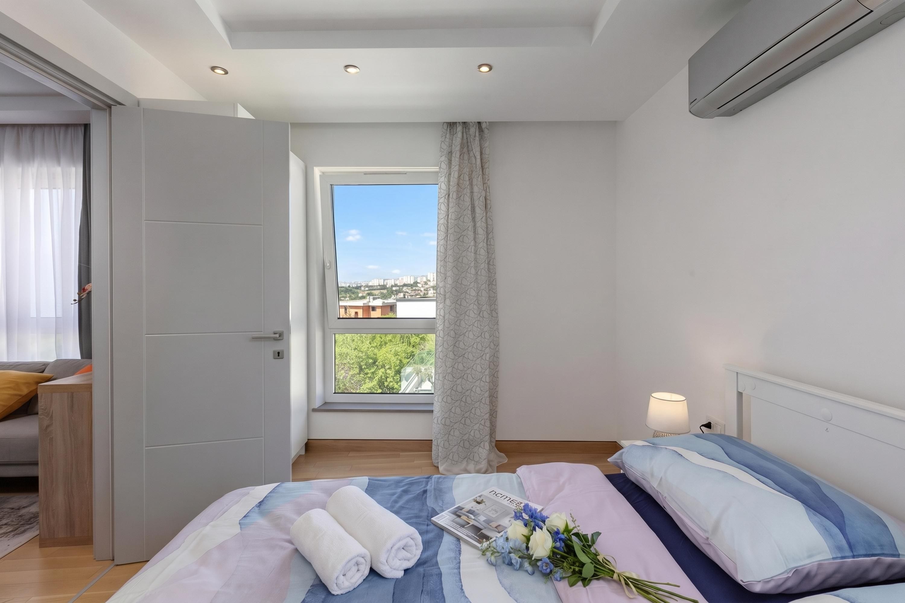 Quarto com cama, janela com vista, porta e ar-condicionado fixado na parede.