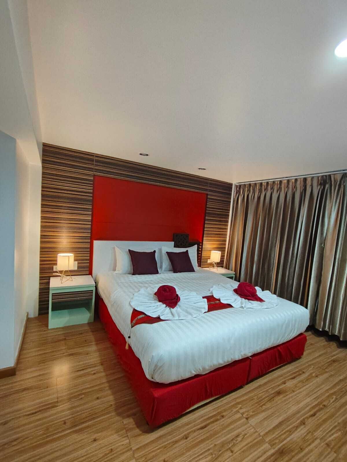 A hotel room with a large bed, a red headboard, and a wooden floor.
