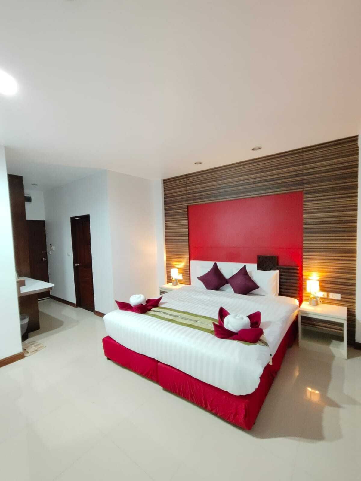 Une chambre d’hôtel moderne avec un grand lit, des touches de couleur rouge et une tête de lit en bois.