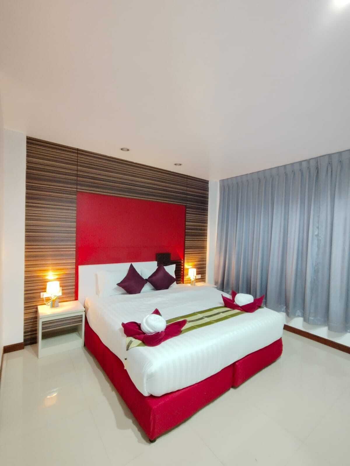 Una habitación de hotel moderna con una cama grande, ropa de cama roja y blanca, un cabecero de madera y una mesita de noche con una lámpara.