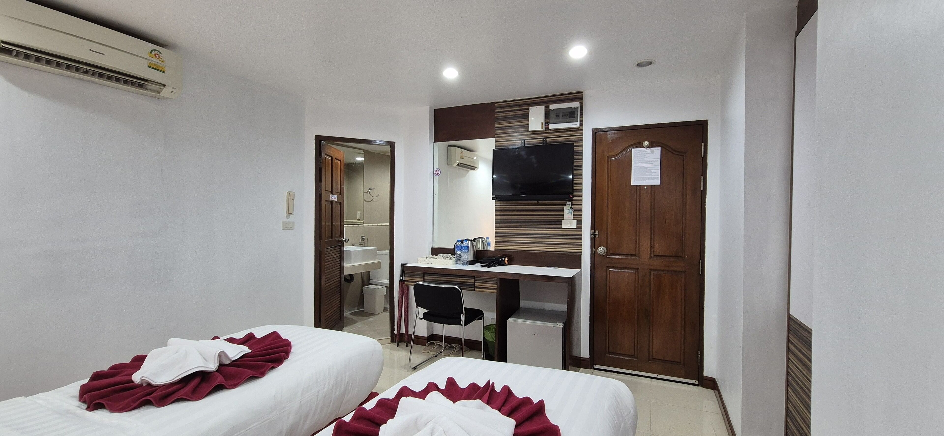 A hotel room with two beds, a desk, a chair, a TV, and a wardrobe.