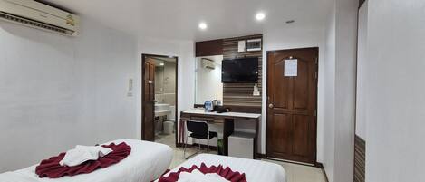 A hotel room with two beds, a desk, a chair, a TV, and a wardrobe.