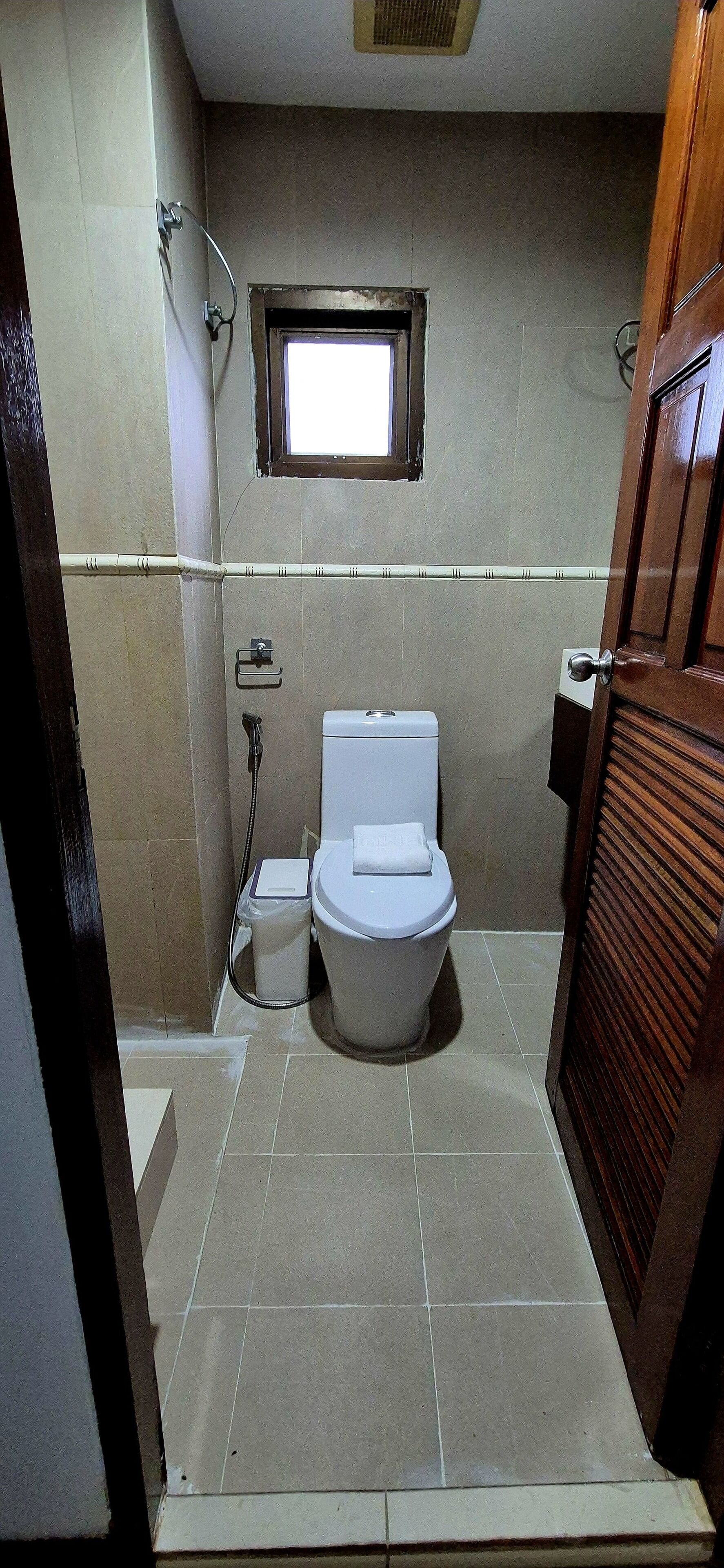 A small, tiled bathroom with a toilet, a shower, and a window.