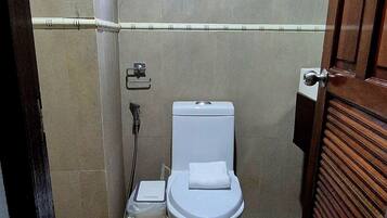 A small, tiled bathroom with a toilet, a shower, and a window.