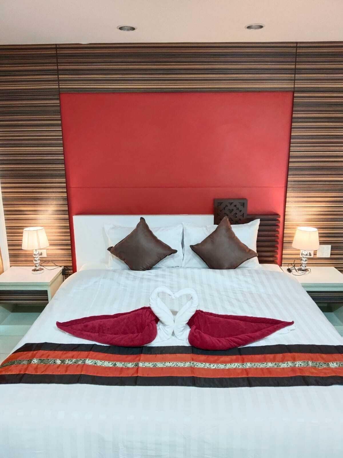 Una habitación de hotel con una cama grande, dos mesitas de noche y un cabecero rojo.