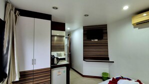Ett kompakt hotellrum med en garderob, ett litet pentry, en säng, en väggmonterad TV och en luftkonditioneringsanläggning.