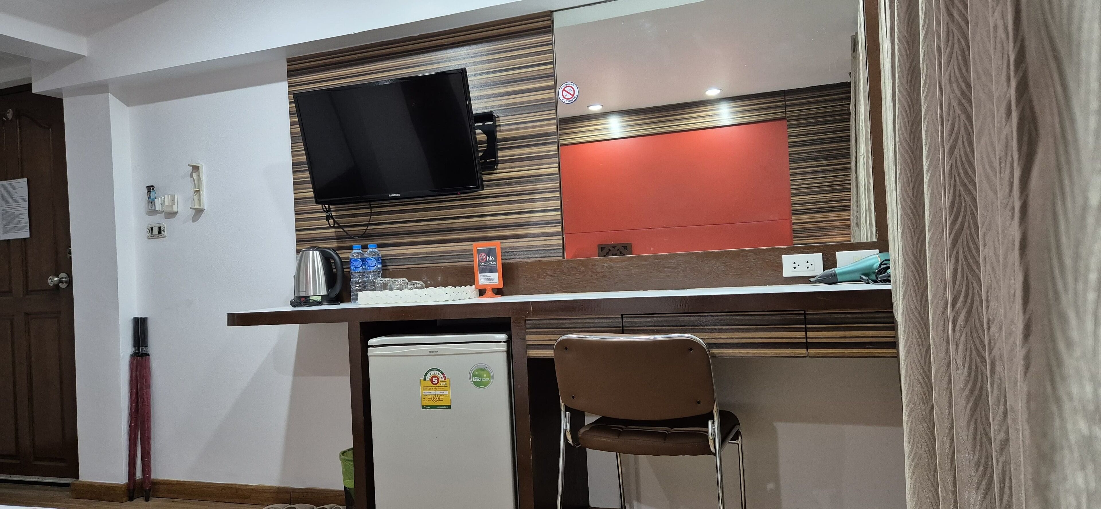 Une chambre d’hôtel compacte comprenant un coin cuisine, un téléviseur à écran plat, un petit réfrigérateur et une seule chaise.