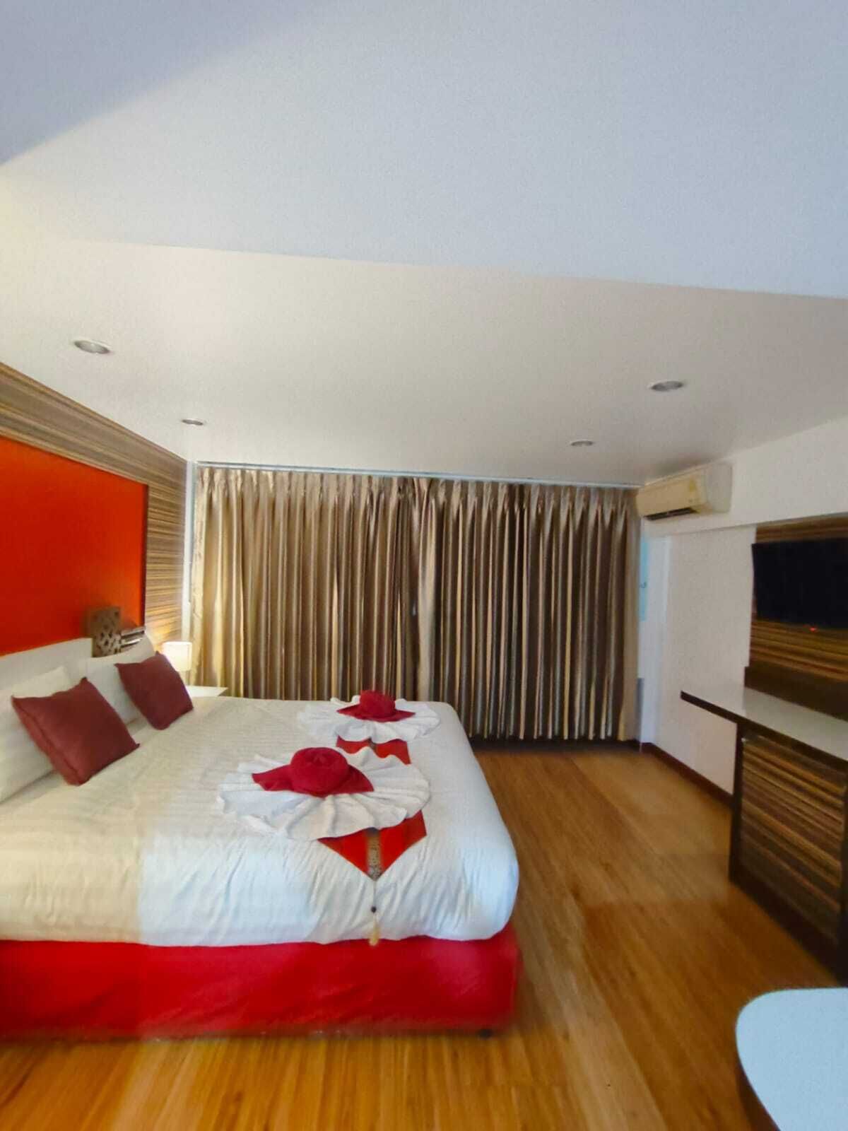 A modern hotel room with a large bed, wooden flooring, a TV, and a curtain.