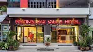Patong Max Value Hotels exteriör har en modern fasad, stora glasfönster och en neonreklamskylt.
