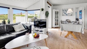 Ein modernes Wohnzimmer mit einer schwarzen Ledersofa, einem weißen Couchtisch mit Obst, einem Fernseher und einem Essbereich mit Tisch für vier Personen.