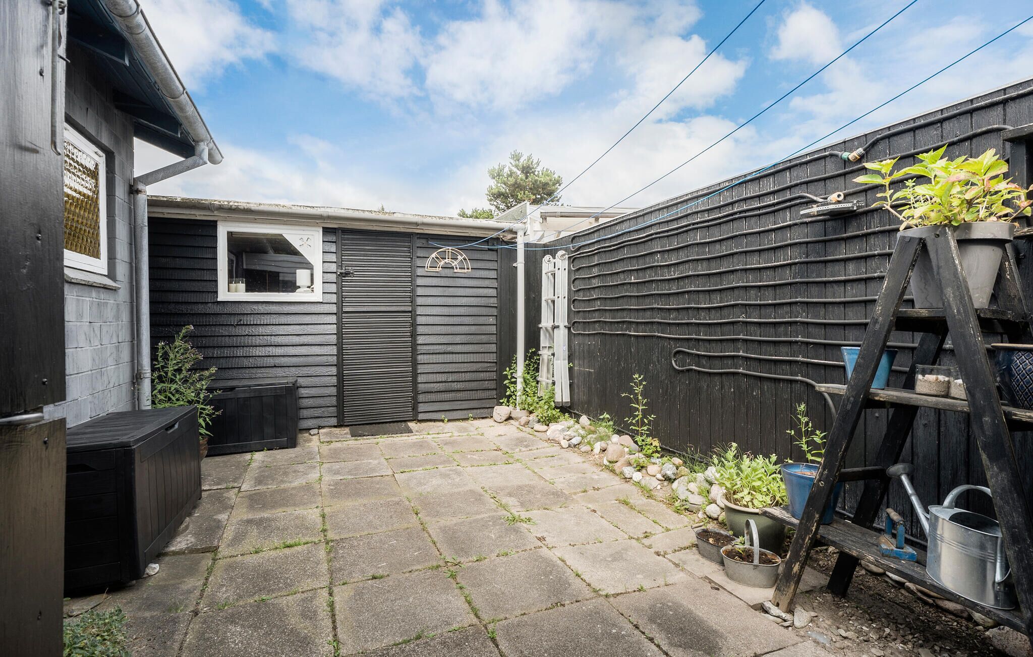 A backyard with a paved patio, a black metal gate, and a wooden fence.