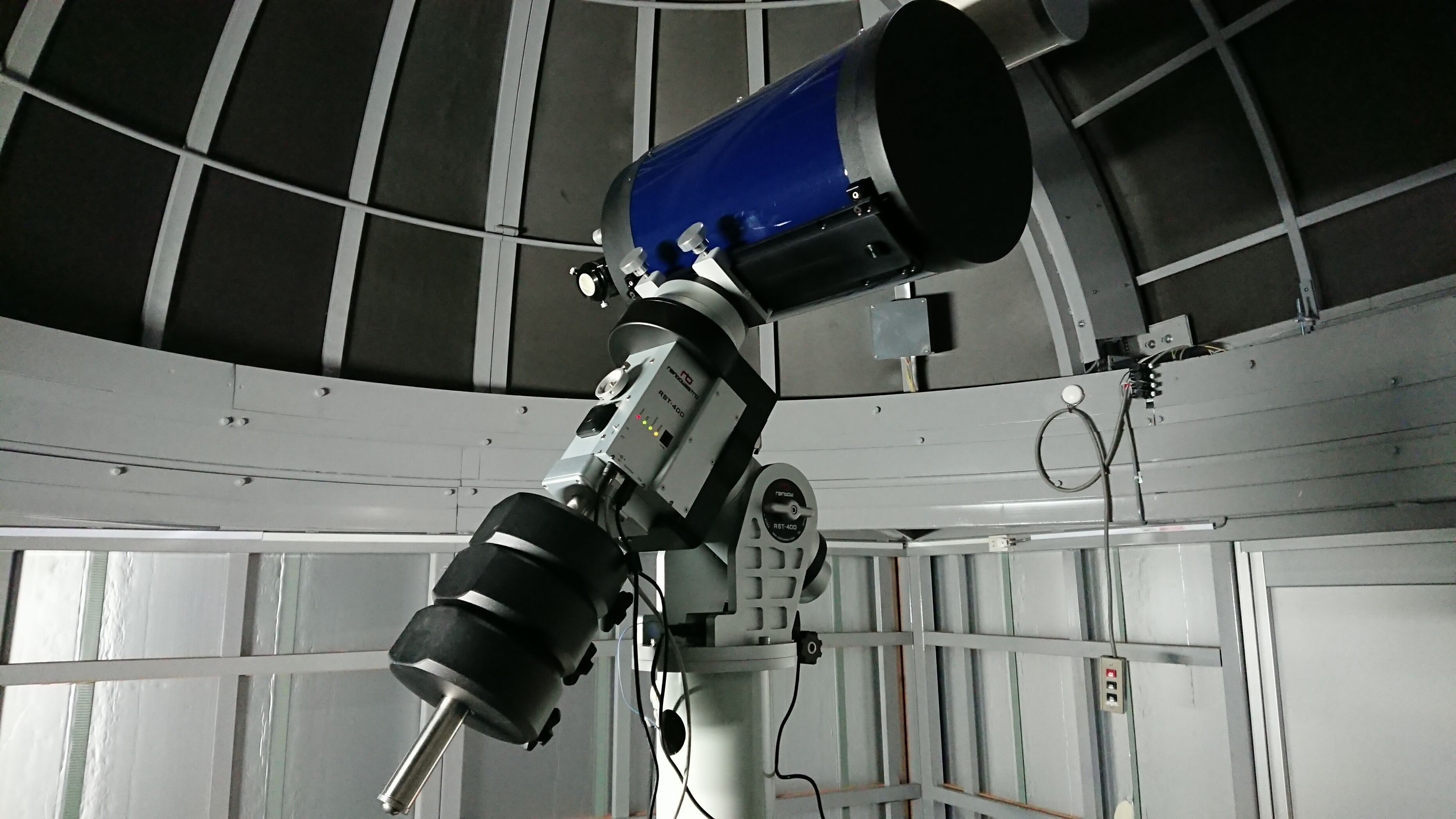Un telescopio montato su un supporto in una stanza con soffitto alto e travi in metallo.