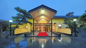 Un bâtiment dont l’entrée est marquée par un tapis rouge, doté d’un espace d’attente abrité, et dont le reflet se mire sur le sol mouillé.