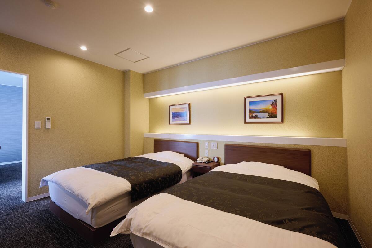 A hotel room with two beds, a nightstand, and a wall-mounted shelf with two framed pictures.