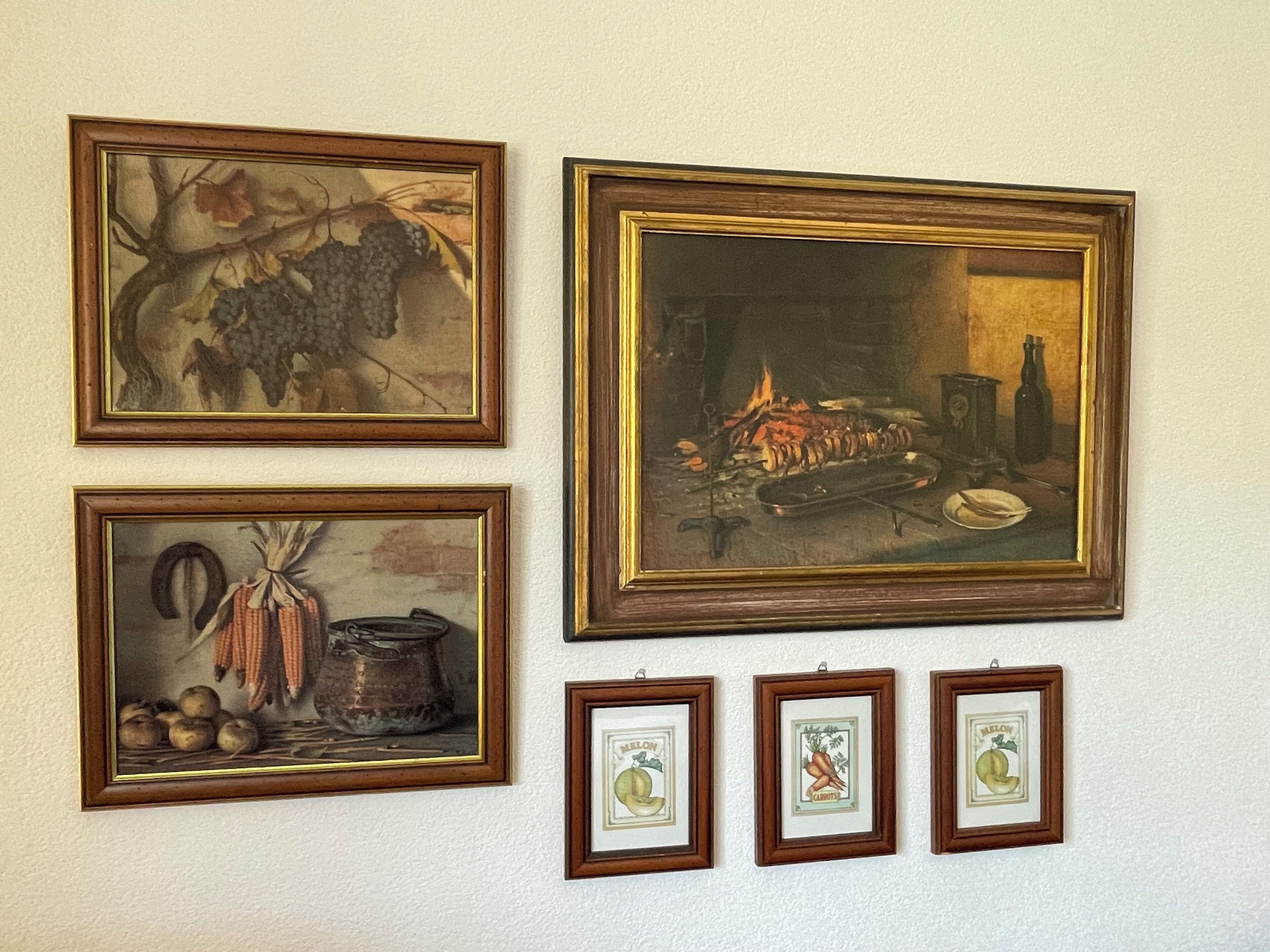 A wall with four framed artworks depicting still life scenes, including grapes, a fire, and vegetables.