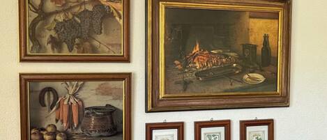 Pared con cuatro cuadros enmarcados que muestran naturalezas muertas, incluyendo uvas, un fuego y verduras.
