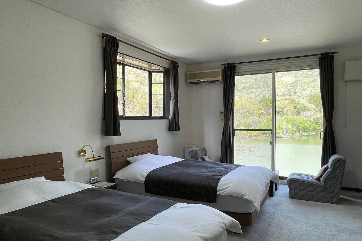 A hotel room with two beds, a chair, and a view of a lake.