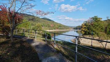 A pathway beside a river with a metal railing, surrounded by trees and hills.