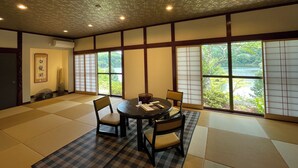 Une pièce de style japonais traditionnel, avec un sol recouvert de tatamis, une table basse entourée de chaises et de grandes fenêtres équipées de panneaux coulissants en papier de riz (shoji).