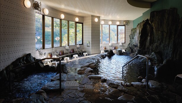 Un espace bien-être doté d’un bain à remous en pierre, de sièges installés au bord de l’eau et de grandes fenêtres offrant une vue sur l’extérieur.