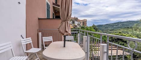 A balcony with a table and chairs, a hanging umbrella, and a view of a hillside.