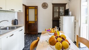 A kitchen with a marble floor, a sink, a coffee maker, a fruit bowl, and a refrigerator.