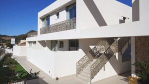 Un bâtiment moderne à deux étages, doté d’une façade blanche, d’un balcon orné d’un délicat travail de ferronnerie et d’un escalier au design similaire.