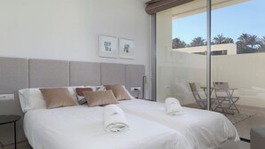Une chambre d’hôtel avec deux lits, une porte vitrée donnant sur un balcon et une petite table avec des chaises.