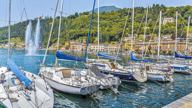 A marina with boats docked, a fountain in the background, and buildings with a yellow facade. - Stunning apartment in Albarè di Costermano with WiFi (Albarè di Costermano)