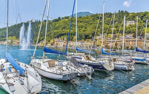 A marina with boats docked, a fountain in the background, and buildings with a yellow facade. - Stunning apartment in Albarè di Costermano with WiFi (Albarè di Costermano)