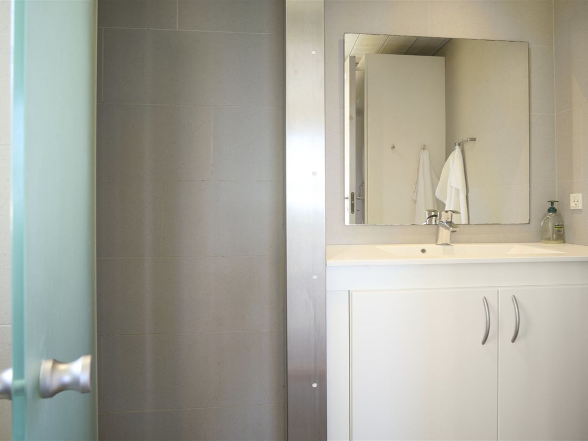 A bathroom with a white sink, a mirror, and a towel hanging on the wall.