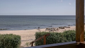 A beach view from a wooden deck with a railing, overlooking a sandy beach with scattered rocks and calm sea.