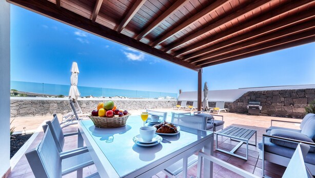 An outdoor dining area with a table set for breakfast, overlooking the beach. - Lanzarote Paradise - Pool, AACC and BBQ By LVH (Playa Blanca)