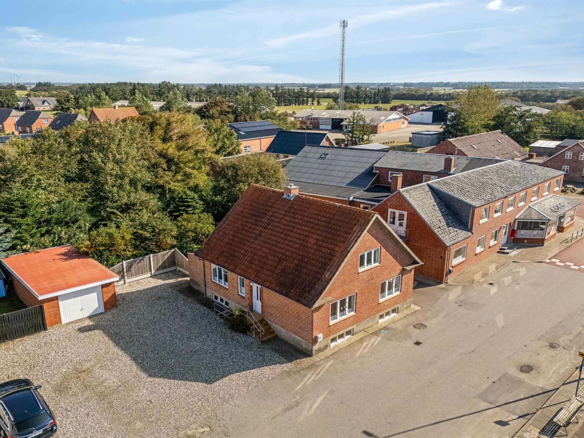 Un quartier résidentiel avec des maisons, une allée gravillonnée et une grande tour de communication en arrière-plan.