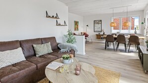 A modern living room with a brown leather sofa, a round coffee table with books and drinks, a dining area with a wooden table and chairs, and a kitchen in the background. - "Ancel" - 1.5km to the fjord by Interhome (Tim)