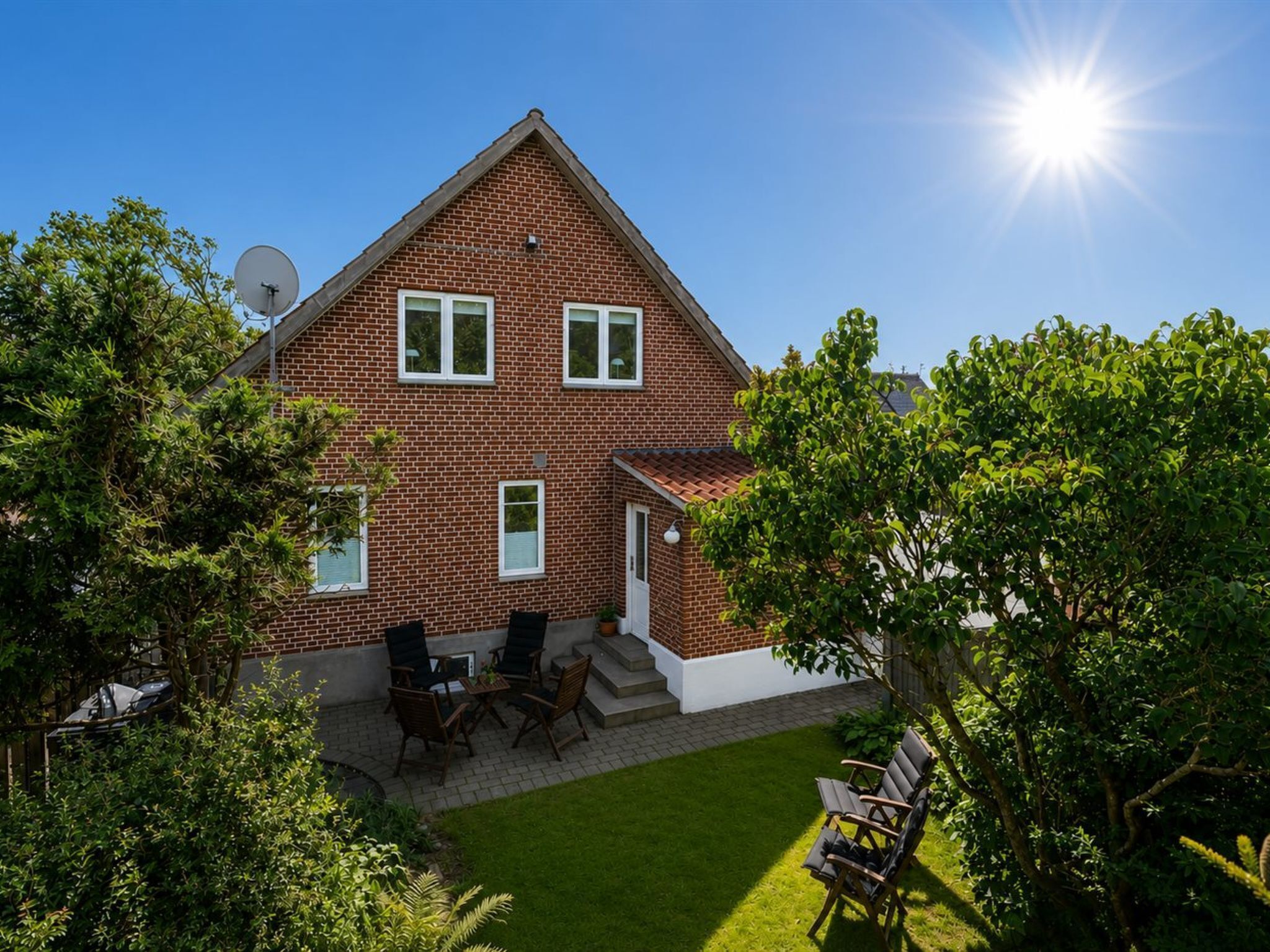 Ein zweistöckiges Backsteinhaus mit einer kleinen Terrasse und Sitzgelegenheiten im Freien.