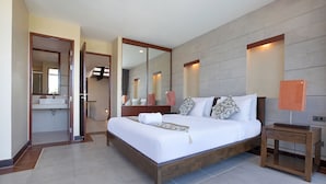Une chambre d’hôtel moderne, dotée d’un grand lit, d’une table de chevet, d’un miroir et d’une salle de bain visible à travers une porte ouverte.