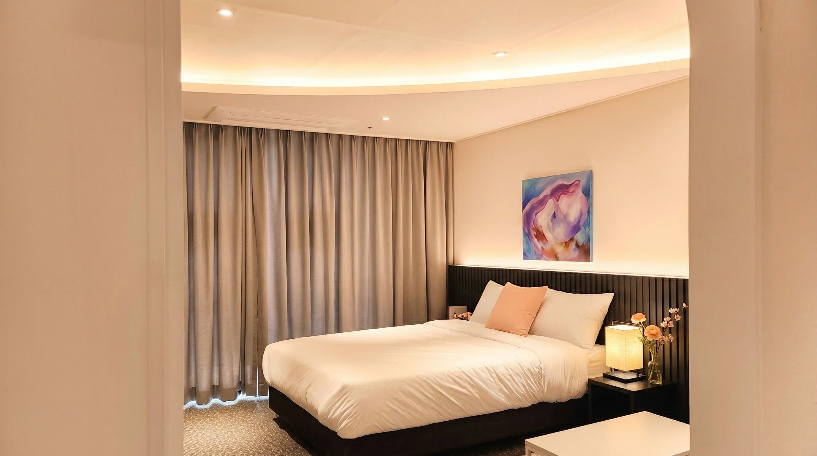A hotel room with a bed, a nightstand with a lamp, and a painting on the wall.